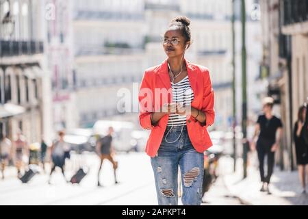 Jeune femme avec écouteurs et smartphone regardant autour dans la ville, Lisbonne, Portugal Banque D'Images