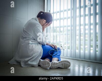 Femme dépressive médecin assis dans le désespoir près d'une fenêtre d'hôpital - concept de soins de santé et de tristesse Banque D'Images