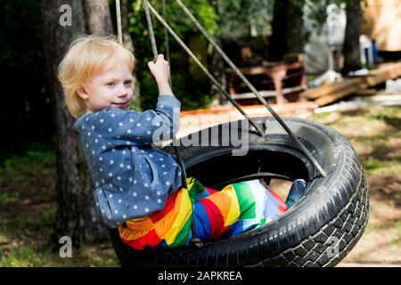 Portrait de la petite fille assise sur la balançoire de pneu Banque D'Images