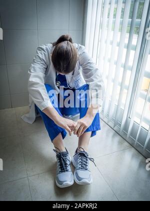 Médecin femme déprimée assise dans le désespoir dans un couloir d'hôpital - concept de soins de santé et de tristesse Banque D'Images