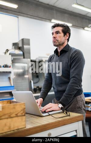 Homme d'affaires pensif utilisant un ordinateur portable dans une usine Banque D'Images
