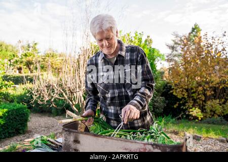 Homme senior qui fait des grillades de légumes dans son jardin Banque D'Images