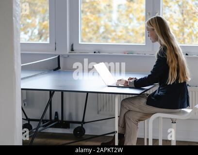 Jeune femme d'affaires utilisant un ordinateur portable sur une table de ping-pong au bureau Banque D'Images