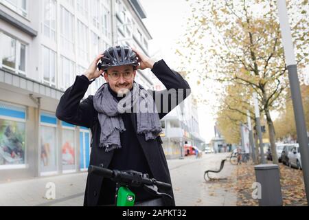 Portrait d'un jeune homme souriant debout sur la chaussée avec un scooter électrique portant un casque de cyclisme Banque D'Images