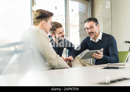 Trois hommes d'affaires ayant une réunion au bureau partageant une tablette Banque D'Images