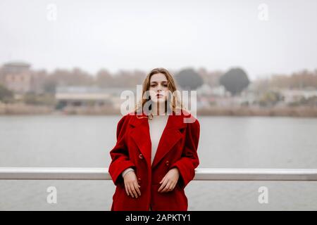 Portrait de la jeune femme portant un manteau rouge, se penchant sur la rampe pendant la journée des pluies Banque D'Images