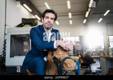 Portrait d'un homme d'affaires sur un cheval à bascule en bois dans une usine Banque D'Images