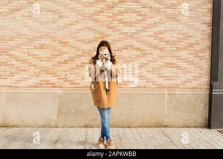 Jeune femme avec appareil photo prenant des photos devant un mur de briques Banque D'Images