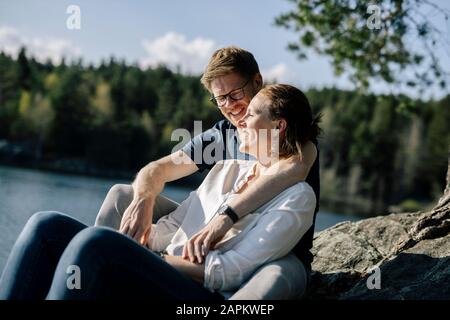 Heureux couple assis sur un rocher au bord du lac, Forstsee, Carinthie, Autriche Banque D'Images