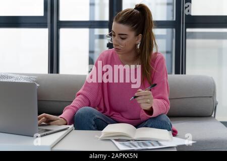 Jeune femme assise sur le canapé travaillant sur ordinateur portable Banque D'Images