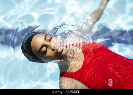 Portrait de la jeune femme avec les yeux fermés flottant sur l'eau dans la piscine Banque D'Images