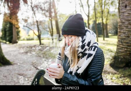Belle blonde femme ayant un café à emporter dans un parc Banque D'Images