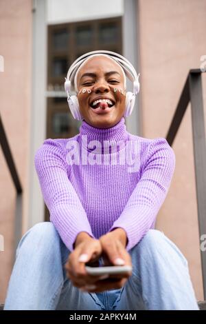 Portrait d'une femme à poil blanc avec un casque blanc et des autocollants sur son visage pour écouter de la musique et sortir de sa langue Banque D'Images