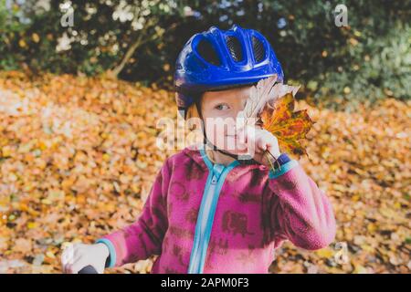 Portrait de la petite fille avec des feuilles d'automne portant un casque de cyclisme bleu Banque D'Images