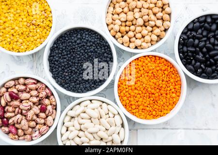 Diverses légumineuses dans les bols : pois chiches, haricots canellini, haricots cailles, haricots noirs, lentilles jaunes, lentilles rouges, lentilles noires Banque D'Images