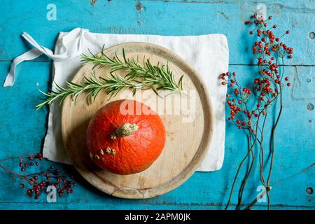 Courge au kuri rouge (Cucurbita maxima), romarin, hanches roses, serviette de table et plaque en bois Banque D'Images