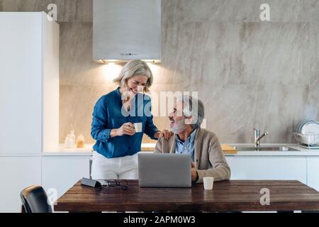 Heureux couple mûr avec ordinateur portable sur table de cuisine à la maison Banque D'Images