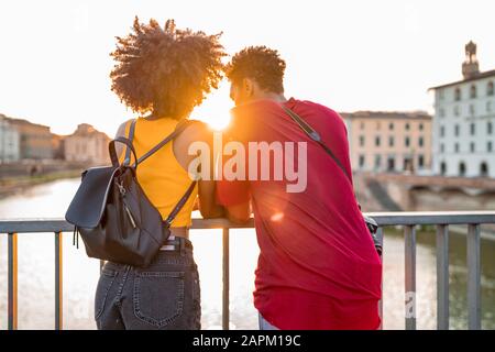 Jeune couple touristique debout sur un pont au-dessus de la rivière Arno au coucher du soleil, Florence, Italie Banque D'Images
