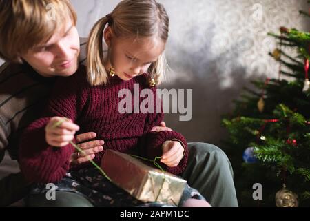 Blonde fille assise sur les genoux du père et ouverture cadeau de Noël Banque D'Images