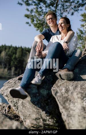 Heureux couple assis sur un rocher au bord du lac, Forstsee, Carinthie, Autriche Banque D'Images