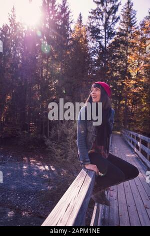 Femme portant un chapeau en laine rouge et une veste denim assise sur une rampe et regardant sur le côté Banque D'Images