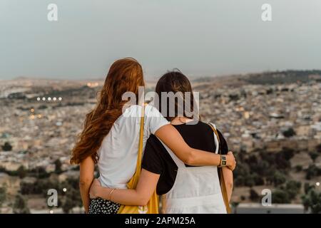 Vue arrière de deux meilleurs amis profitant de la vue sur la ville bras dans le soir, Fez, Maroc Banque D'Images