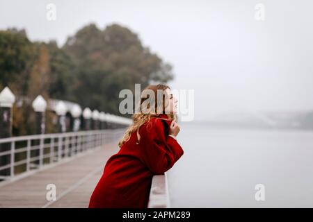 Portrait de la jeune femme portant un manteau rouge, se penchant sur la rampe le jour de la pluie Banque D'Images