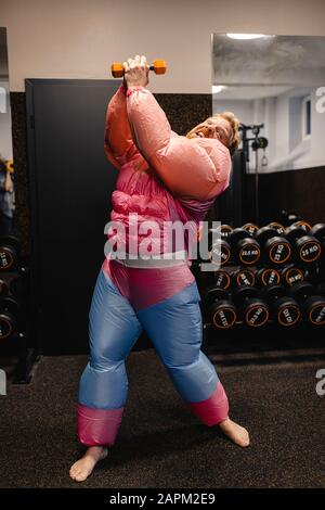 Homme dans la salle de gym portant un bodybuilder rose costume levage haltère Banque D'Images