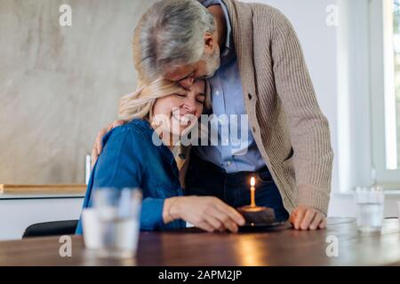 Couple d'âge mûr célébrant l'anniversaire avec gâteau dans la cuisine à la maison Banque D'Images