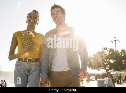 Un jeune couple heureux marchant au bord de l'eau au coucher du soleil, Lisbonne, Portugal Banque D'Images