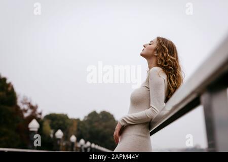 Portrait de la jeune femme portant une robe blanche, se penchant sur la rampe le jour de la pluie Banque D'Images