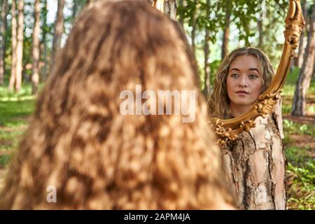 Vue arrière de la jeune femme regardant son image miroir dans une forêt Banque D'Images