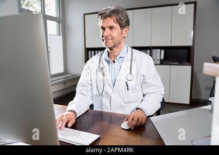 Médecin utilisant l'ordinateur au bureau dans sa pratique médicale Banque D'Images