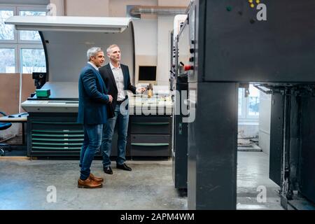 Deux hommes d'affaires regardant une machine dans une usine Banque D'Images