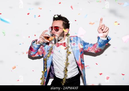 Un homme cool et élégant portant un costume coloré et des lunettes de soleil célébrant une fête avec des confettis et de la boisson Banque D'Images