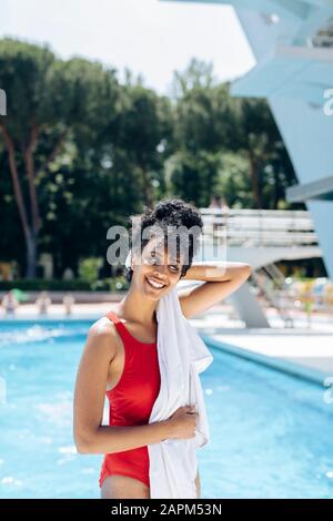 Portrait d'une jeune femme souriante dans une combinaison de bain rouge qui s'est remorchée devant une piscine Banque D'Images