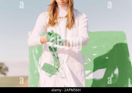 Jeune femme sur terrain sec, peinture toile avec peinture verte Banque D'Images