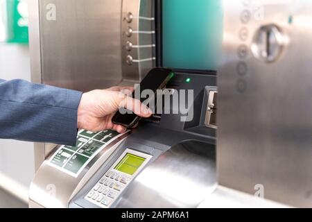 Homme tenant son smartphone sur la machine à billets et payant Banque D'Images