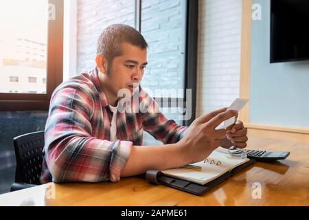 Homme asiatique qui calcule les absences, essaie de résoudre les problèmes budgétaires, regarde les documents, gérer avec les factures de services publics. Banque D'Images