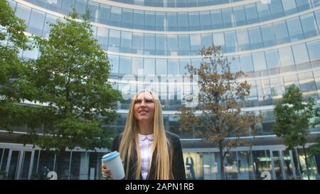 Par en dessous de la blonde woman in suit le café dans la tasse de papier à l'écart sur rue. Banque D'Images