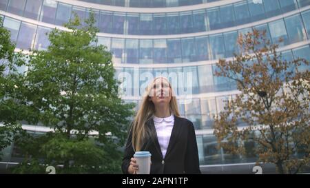 Par en dessous de la blonde woman in suit le café dans la tasse de papier à l'écart sur rue. Banque D'Images