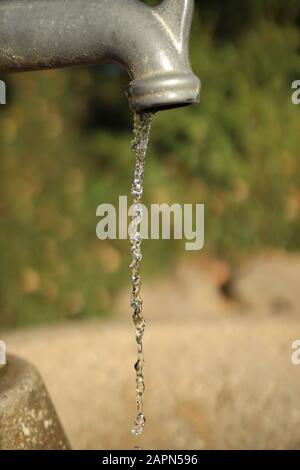 Gros plan vertical d'un robinet gris avec de l'eau goutte à goutte un flou en arrière-plan Banque D'Images