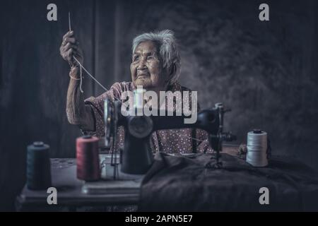 Jolie femme âgée de 90 ans utilisant une machine à coudre d'époque. Adorable femme âgée à coudre des vêtements dans sa vieille maison familiale. Banque D'Images