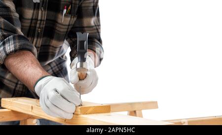 Gros plan. Carpenter avec ses mains protégées par des gants avec marteau et clous fixe une planche en bois. Industrie de la construction. Fond blanc. Banque D'Images