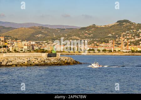 Vue panoramique sur la ville côtière d'Oneglia, Riviera des fleurs, avec un bateau passant devant le phare vert dans une journée ensoleillée, Imperia, Italie Banque D'Images