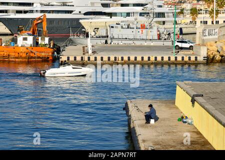 Vue imprenable sur le port avec un pêcheur âgé sur le quai, un vedettes et yachts de luxe, Porto Maurizio, Imperia, Ligurie, Italie Banque D'Images