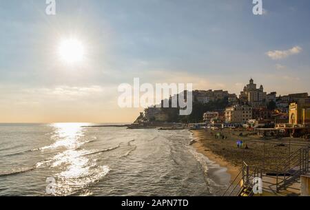 Vue rétro-éclairée sur la plage de sable de Porto Maurizio avec l'arrondissement de Parasio sur le promontoire en hiver ensoleillé, Imperia, Ligurie, Italie Banque D'Images