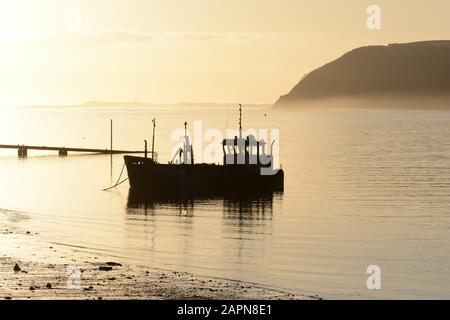 Vieux bateau de pêche silhouetted dans misty début de soirée coucher de soleil coucher de soleil Tywi Estuaire Ferryside Carmarthenshire Pays de Galles Cymru Royaume-Uni Banque D'Images