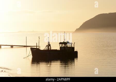 Vieux bateau de pêche silhouetted dans misty début de soirée coucher de soleil coucher de soleil Tywi Estuaire Ferryside Carmarthenshire Pays de Galles Cymru Royaume-Uni Banque D'Images