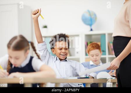 Un écolier africain assis à son bureau et heureux avec une bonne note tandis que l'enseignant lui montrant le papier dans la salle de classe Banque D'Images